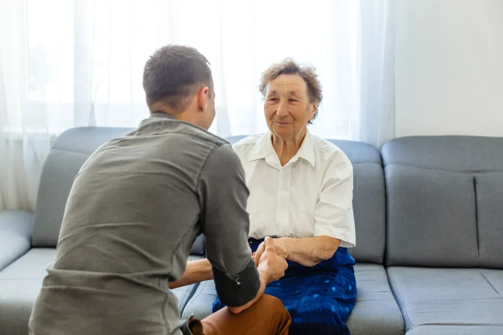 Caregiver assisting elderly woman on sofa