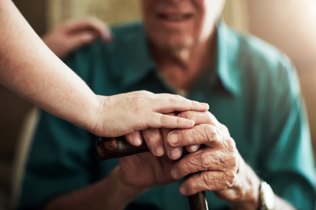 Carer placing hand on elderly man's hands