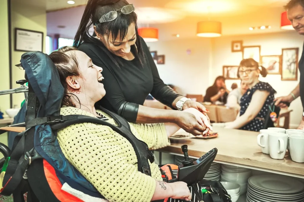 Carer laughing with client in wheelchair at café