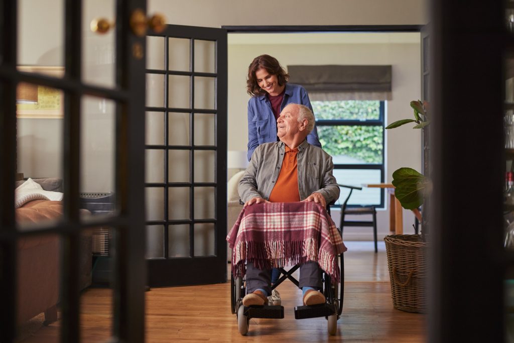 Carer assisting elderly man in wheelchair at home